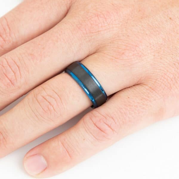 A ring finger wearing The Hayes with its black brushed center and blue polished edges and sleeve.