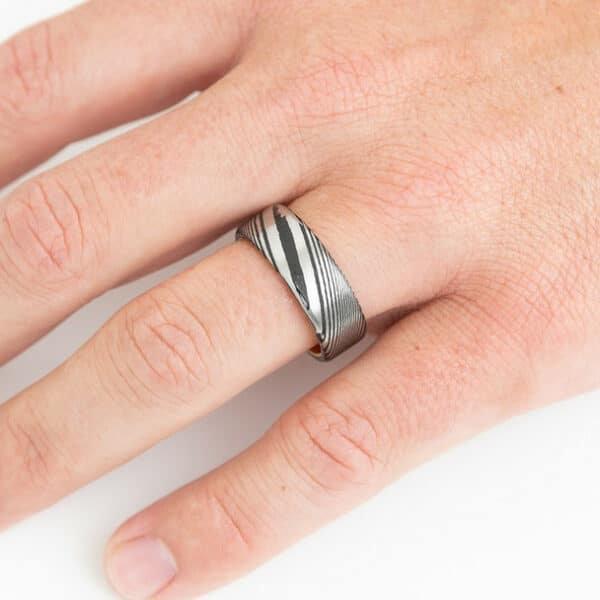 A hand wearing an 8mm Damascus steel ring on the ring finger.